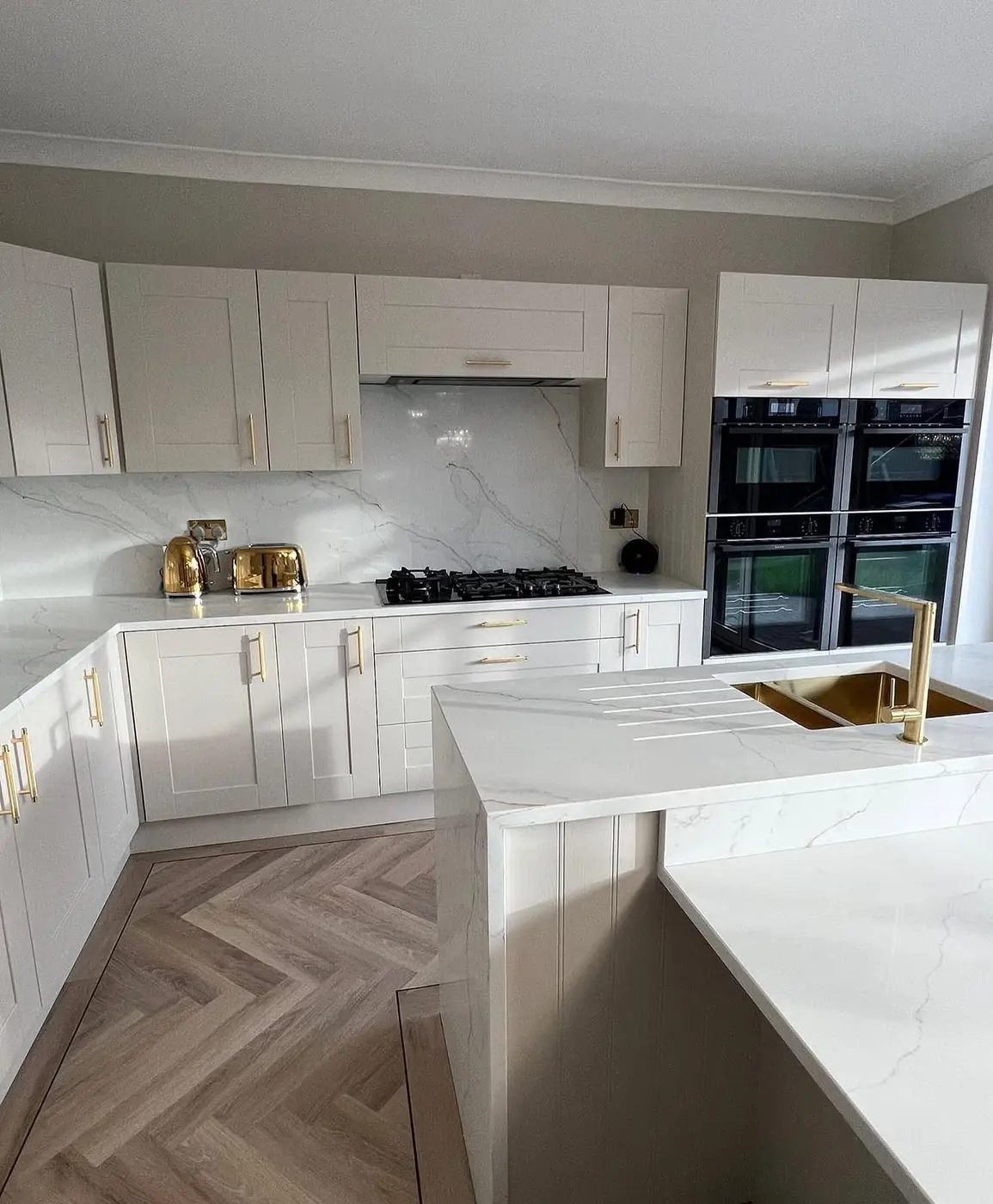 White shaker kitchen with brass tap and range of built-in ovens