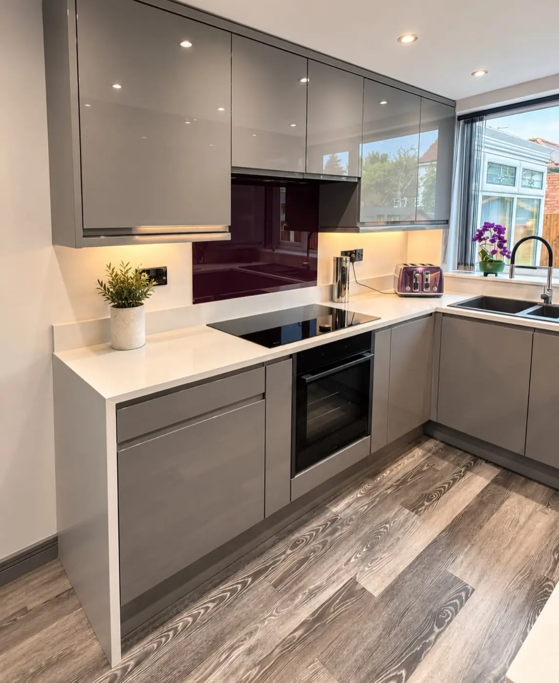 Gloss grey kitchen with plum glass splashback and white worktops